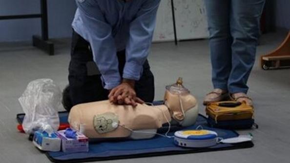 A person applying CPR to the CPR doll on the floor while a person looks on
